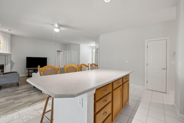 kitchen featuring a breakfast bar, light countertops, a tiled fireplace, a kitchen island, and ceiling fan