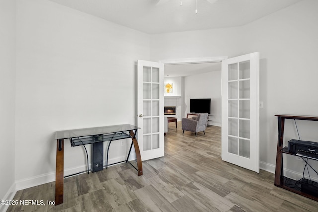 interior space with a lit fireplace, baseboards, wood finished floors, and french doors