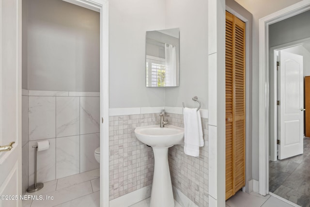 bathroom with toilet, a wainscoted wall, tile walls, a closet, and tile patterned floors