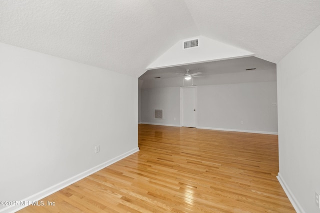 additional living space featuring visible vents, light wood-style floors, vaulted ceiling, a textured ceiling, and baseboards