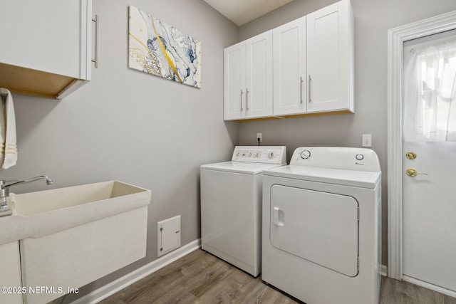 washroom featuring a sink, wood finished floors, washing machine and dryer, and cabinet space