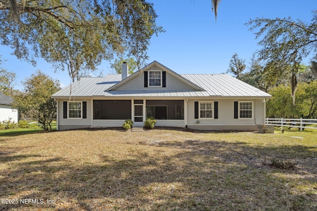 view of front of property featuring metal roof, fence, a sunroom, a chimney, and a front yard