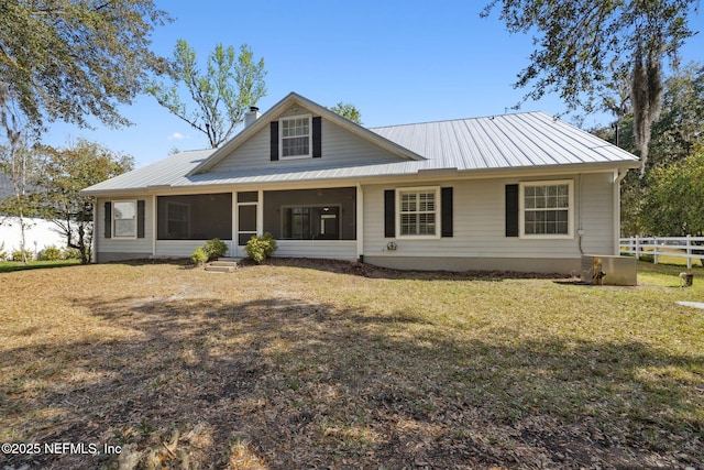 rear view of property with metal roof, fence, a sunroom, a lawn, and a chimney