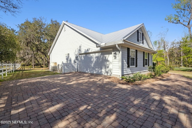 view of property exterior with metal roof, decorative driveway, an attached garage, and fence