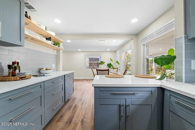 kitchen with a peninsula, wood finished floors, light countertops, backsplash, and open shelves