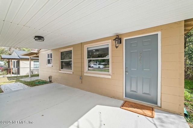 view of exterior entry featuring concrete block siding, a patio area, and fence