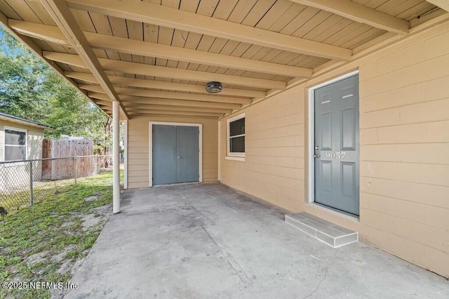 view of exterior entry with concrete block siding, a patio area, and fence