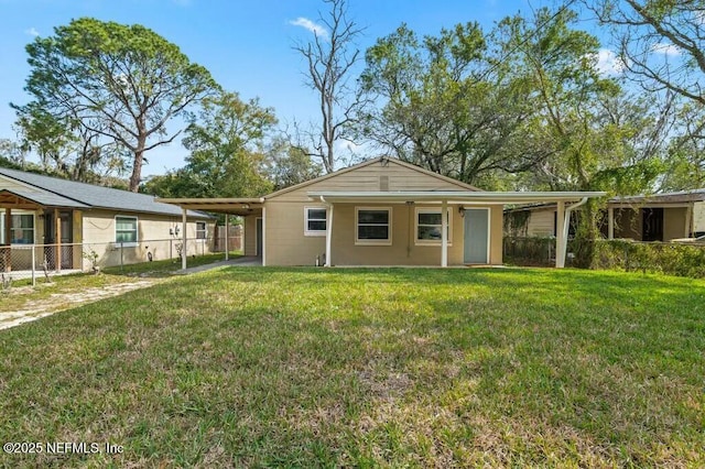 rear view of house featuring a carport, fence, and a lawn