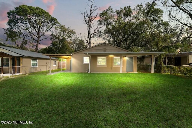 back of property at dusk with a yard, a carport, and fence