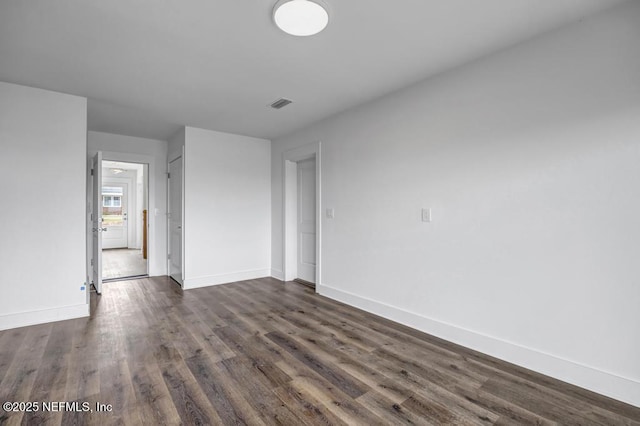 unfurnished room featuring dark wood-style flooring, visible vents, and baseboards