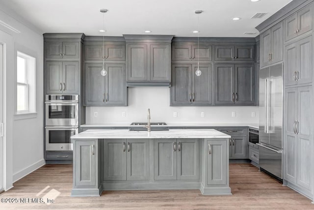 kitchen with light wood finished floors, visible vents, an island with sink, appliances with stainless steel finishes, and hanging light fixtures