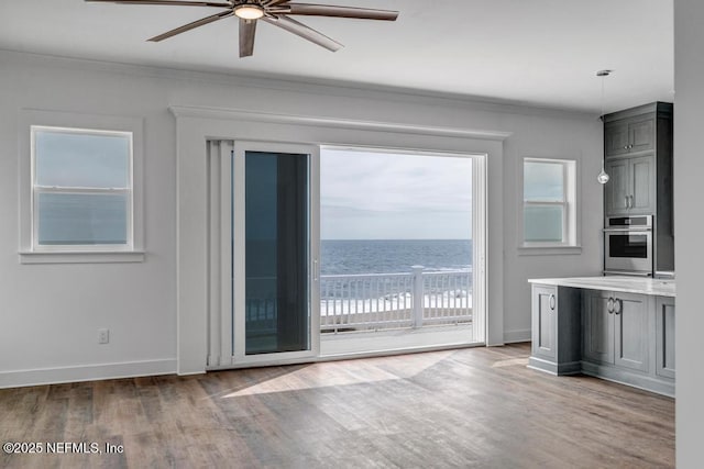 interior space with ceiling fan, a water view, wood finished floors, and baseboards