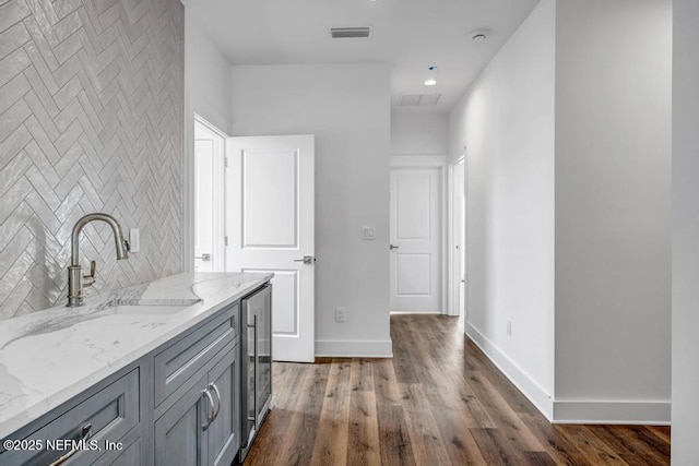 interior space featuring wine cooler, visible vents, a sink, wood finished floors, and baseboards