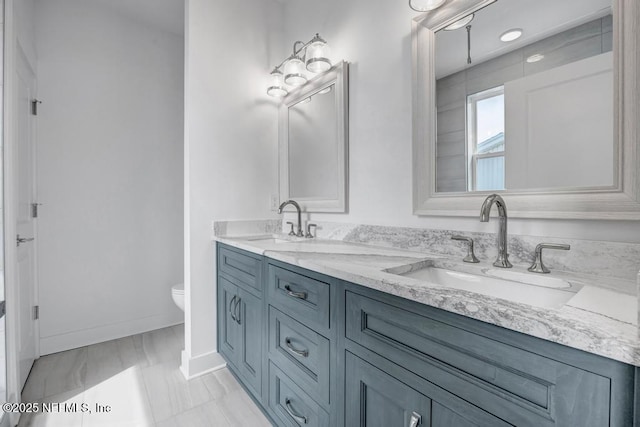 bathroom with baseboards, a sink, toilet, and double vanity