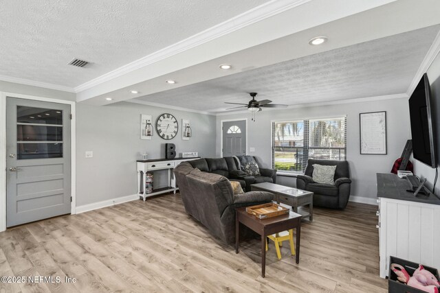 living area featuring visible vents, baseboards, ornamental molding, light wood-style floors, and a textured ceiling