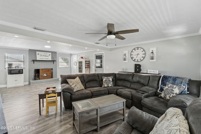 living area featuring visible vents, light wood-style flooring, a fireplace, crown molding, and ceiling fan