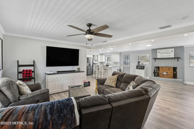 living room with visible vents, ceiling fan, ornamental molding, a brick fireplace, and light wood-type flooring