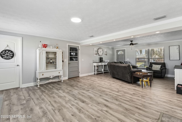 living room with baseboards, visible vents, light wood-style flooring, a textured ceiling, and crown molding