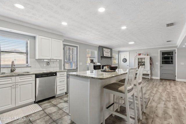 kitchen featuring visible vents, a sink, dishwasher, crown molding, and a brick fireplace