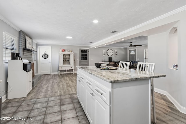 kitchen featuring visible vents, a center island, ornamental molding, a kitchen breakfast bar, and white cabinetry