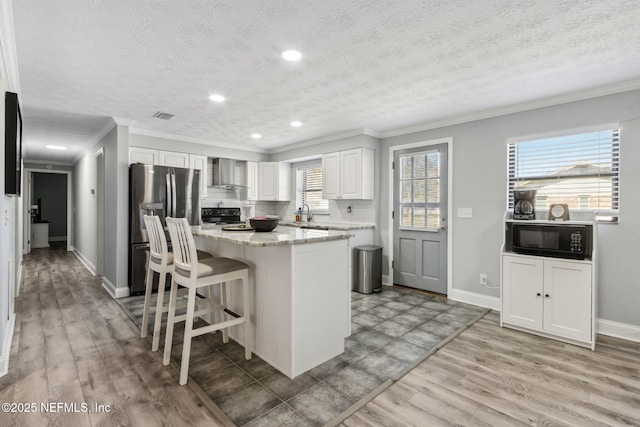 kitchen featuring a center island, a kitchen bar, light wood-style flooring, black appliances, and wall chimney exhaust hood