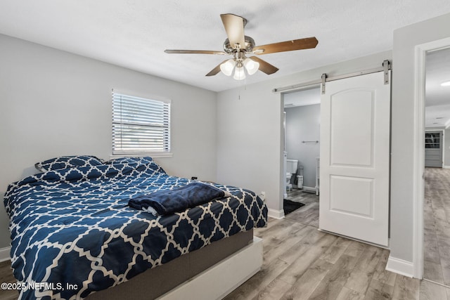 bedroom with a barn door, baseboards, light wood-style floors, and ceiling fan