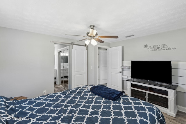 bedroom featuring a ceiling fan, a barn door, wood finished floors, and visible vents