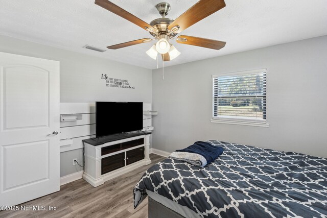 bedroom with visible vents, ceiling fan, baseboards, wood finished floors, and a textured ceiling