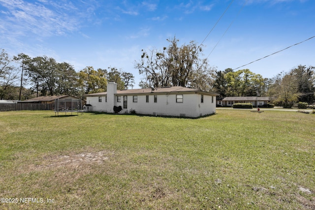 back of house with a trampoline, a lawn, and fence