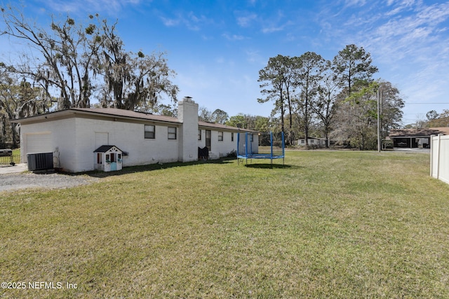 view of yard featuring a garage, a trampoline, and central AC