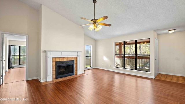 unfurnished living room with ceiling fan, a textured ceiling, a tiled fireplace, and wood finished floors