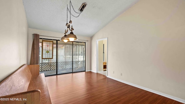 unfurnished dining area with lofted ceiling, a textured ceiling, baseboards, and wood finished floors