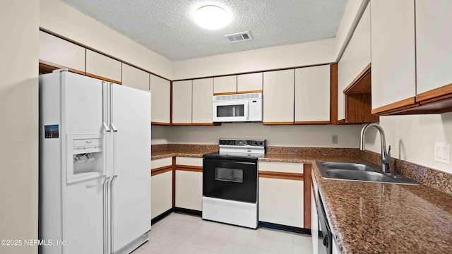 kitchen featuring dark countertops, visible vents, a sink, a textured ceiling, and white appliances