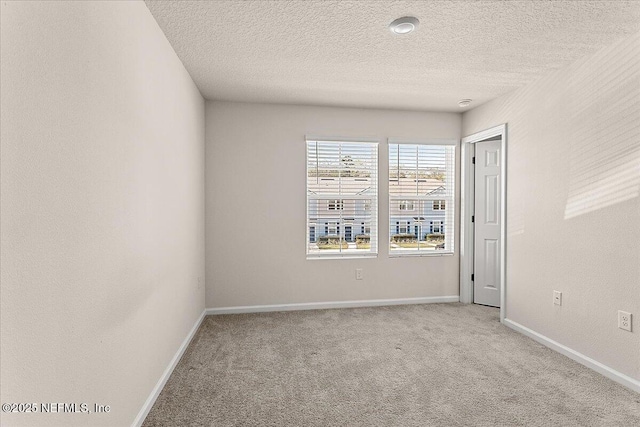 spare room with a textured ceiling, carpet flooring, and baseboards