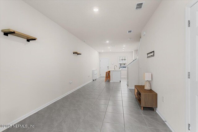 hallway with light tile patterned floors, recessed lighting, a sink, visible vents, and baseboards