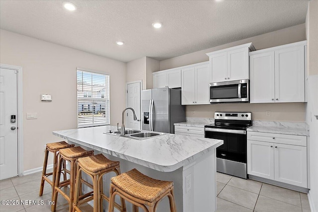 kitchen featuring light tile patterned floors, a kitchen island with sink, a sink, light countertops, and appliances with stainless steel finishes