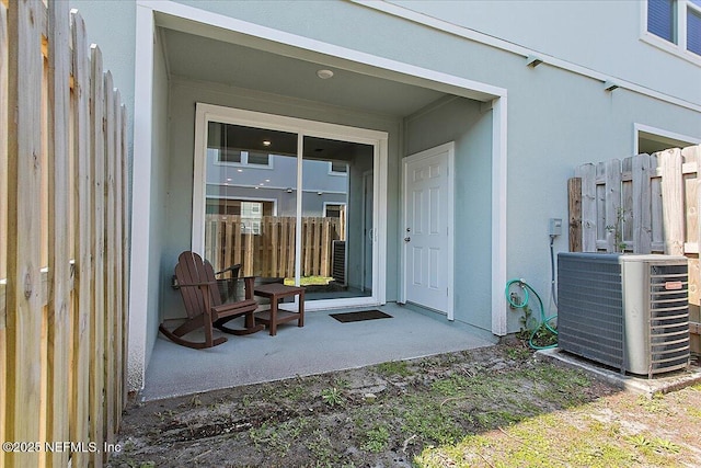 view of exterior entry with stucco siding, fence, and central AC unit