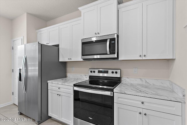 kitchen featuring a textured ceiling, light tile patterned floors, light stone counters, white cabinetry, and appliances with stainless steel finishes