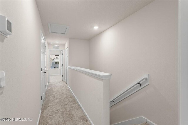 hall featuring visible vents, baseboards, an upstairs landing, carpet, and attic access