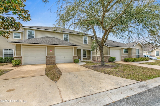 townhome / multi-family property featuring a shingled roof, brick siding, driveway, and an attached garage