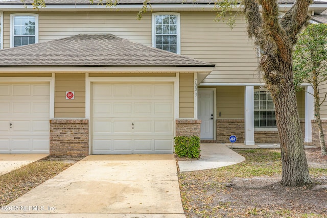 view of front of home with roof with shingles, driveway, brick siding, and an attached garage