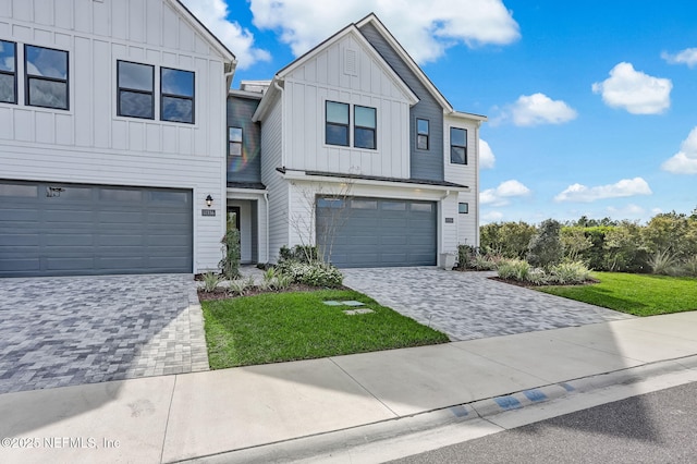 view of front facade with decorative driveway, board and batten siding, an attached garage, and a front lawn