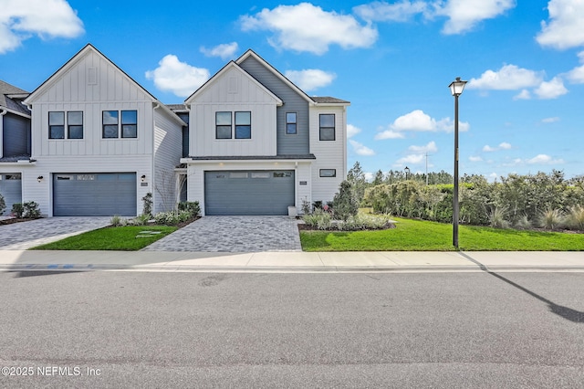 view of front of property with board and batten siding, decorative driveway, a front lawn, and a garage