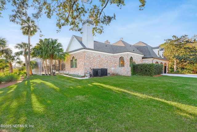 exterior space featuring central AC unit, brick siding, concrete driveway, a front lawn, and a chimney