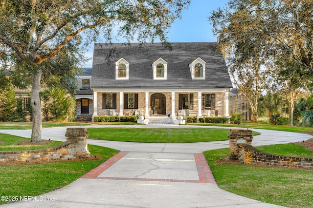 cape cod home with decorative driveway, covered porch, and a front lawn