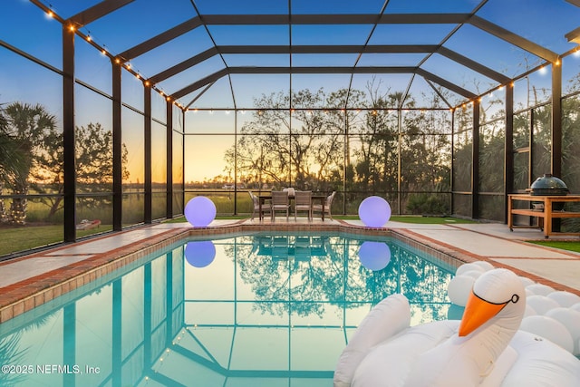 pool at dusk featuring glass enclosure, a patio area, and an outdoor pool