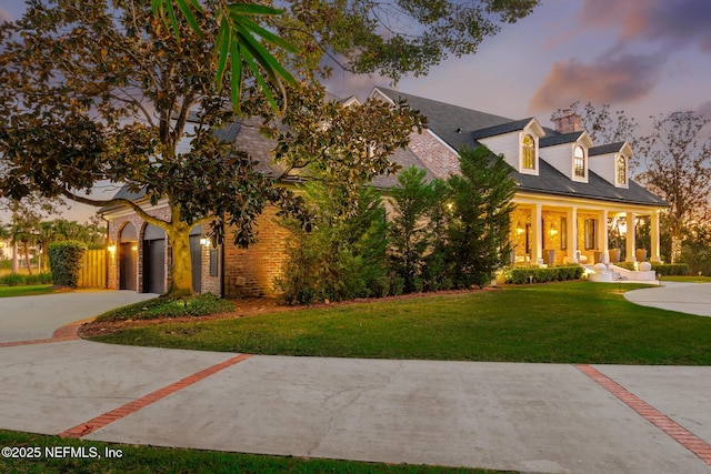 cape cod house featuring brick siding, covered porch, concrete driveway, and a yard