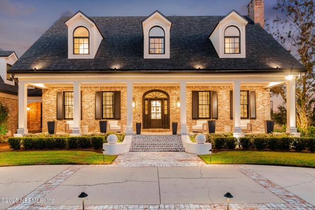 view of front of house featuring brick siding, a chimney, a porch, and a shingled roof