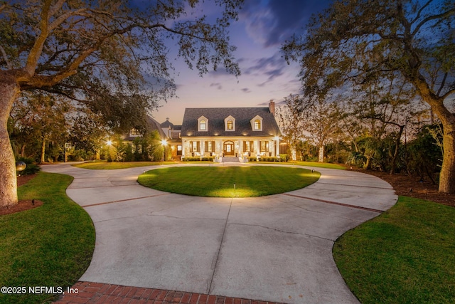 cape cod home featuring curved driveway, a chimney, and a lawn