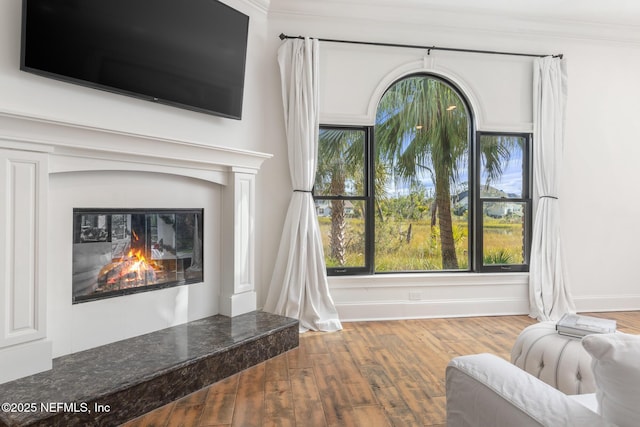 living room with ornamental molding, a glass covered fireplace, baseboards, and wood finished floors